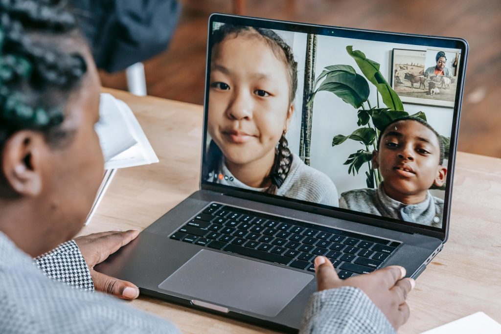 A young black child having a virtual English Second Language class on her laptop with two other light-skinned africans shown on the laptop screen