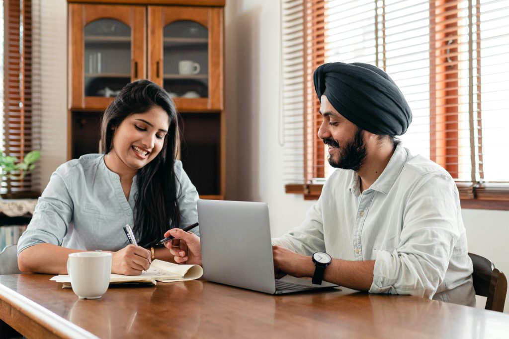  A desi man and woman seated at a desk taking virtual English lessons together.