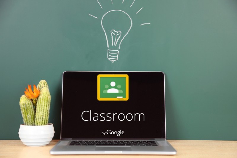 A laptop in front of a blackboard with the title ''Google Classroom'' on the screen.